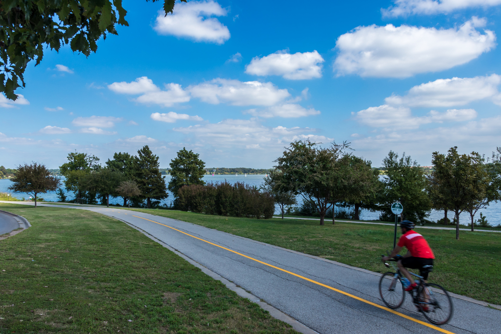 Lone,Male,Cyclist,On,A,Bike,Trail,With,Lake,And